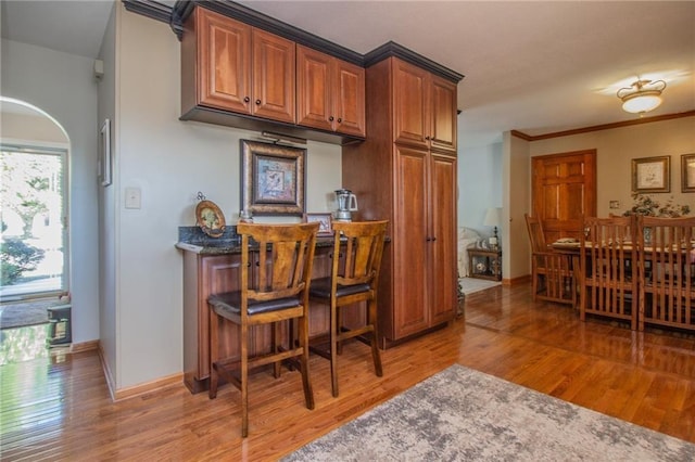 kitchen featuring baseboards, brown cabinets, ornamental molding, and light wood finished floors