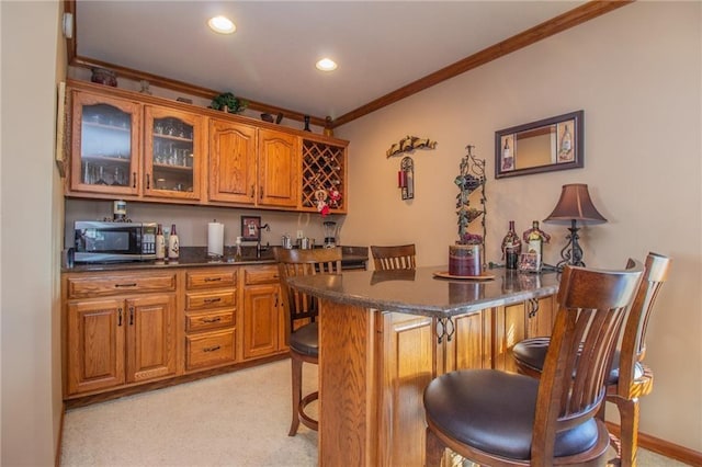 kitchen with brown cabinetry, crown molding, glass insert cabinets, stainless steel microwave, and a kitchen breakfast bar