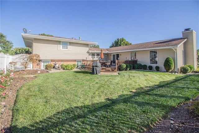 back of property featuring a chimney, a wooden deck, a yard, and fence