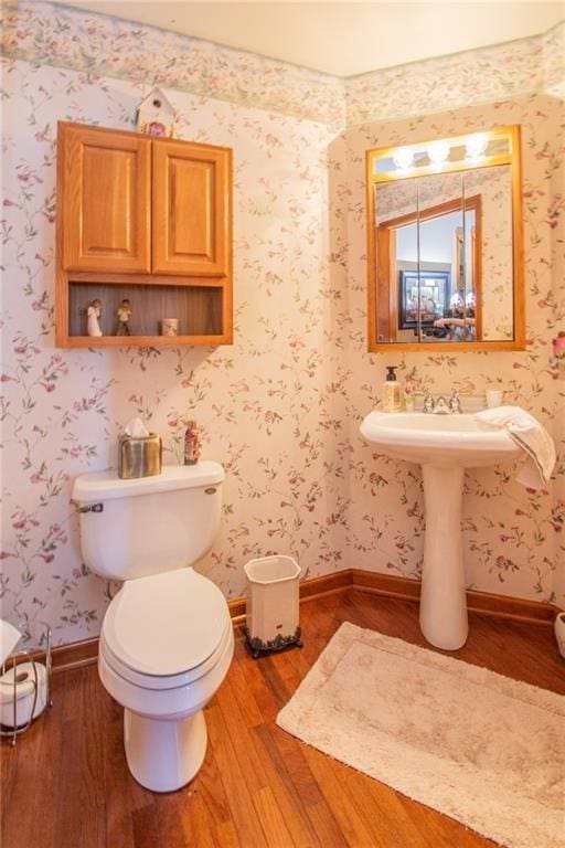 bathroom featuring toilet, wallpapered walls, baseboards, and wood finished floors