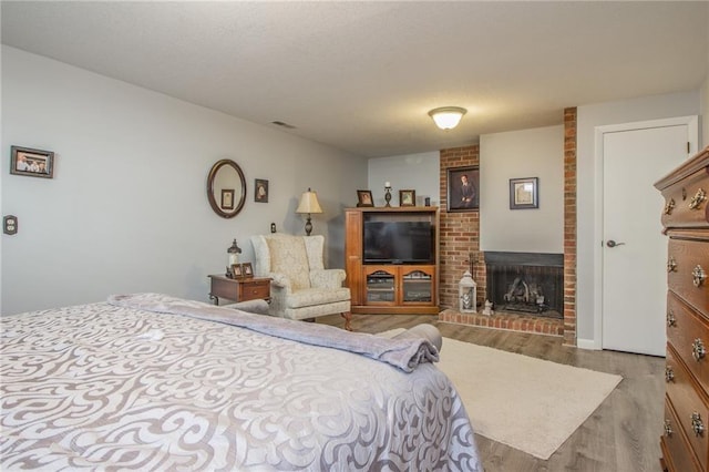 bedroom featuring a brick fireplace, a textured ceiling, and wood finished floors