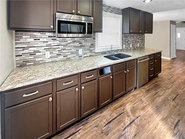 kitchen featuring dark brown cabinetry, light stone counters, wood finished floors, stainless steel appliances, and a sink