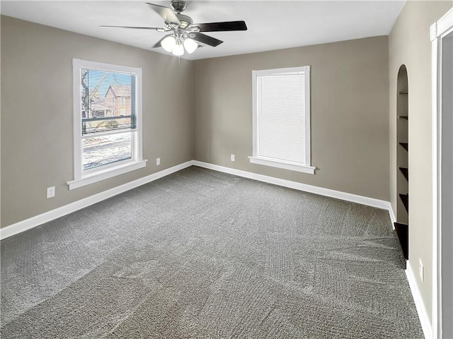 carpeted empty room with ceiling fan, baseboards, and arched walkways