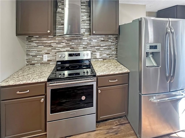 kitchen with light wood finished floors, decorative backsplash, light stone counters, appliances with stainless steel finishes, and wall chimney range hood