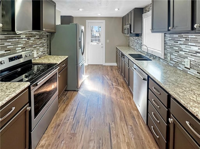 kitchen featuring stainless steel appliances, wood finished floors, a sink, and light stone countertops