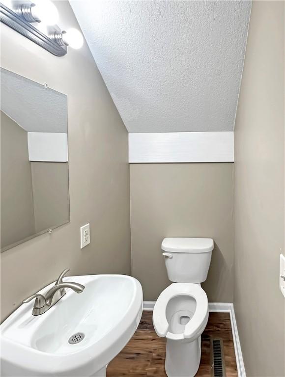 bathroom with vaulted ceiling, a sink, a textured ceiling, wood finished floors, and baseboards