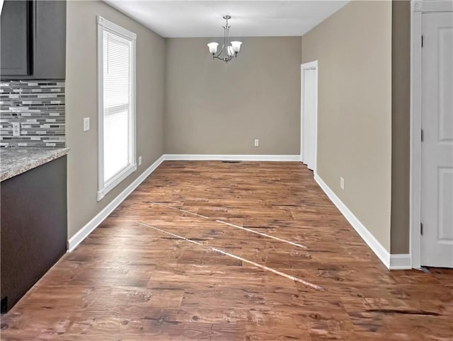 unfurnished dining area featuring dark wood-style floors, a chandelier, and baseboards