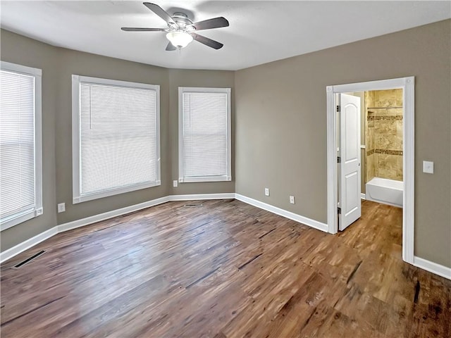 empty room with a ceiling fan, wood finished floors, visible vents, and baseboards