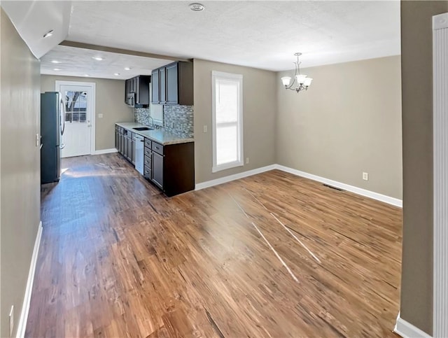 kitchen featuring wood finished floors, a sink, baseboards, backsplash, and freestanding refrigerator