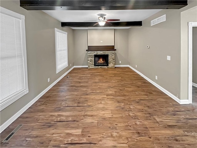 unfurnished living room with visible vents, beamed ceiling, a stone fireplace, and baseboards