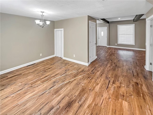 unfurnished room featuring visible vents, a notable chandelier, baseboards, and wood finished floors