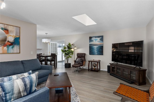 living area featuring a skylight, wood finished floors, an inviting chandelier, and baseboards