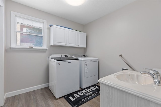 clothes washing area featuring a sink, light wood-style floors, baseboards, cabinet space, and washing machine and clothes dryer