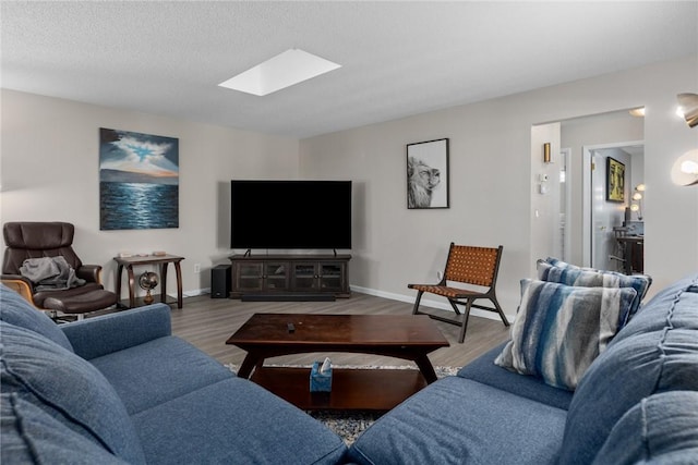 living room with a skylight, a textured ceiling, baseboards, and wood finished floors