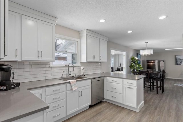 kitchen featuring a sink, a peninsula, white cabinets, and stainless steel dishwasher