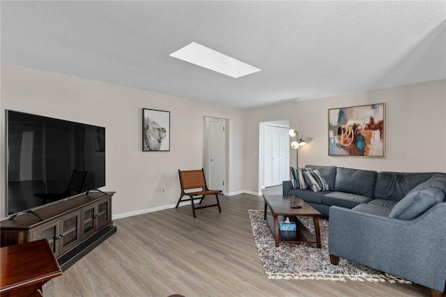 living room featuring a skylight, a textured ceiling, baseboards, and wood finished floors