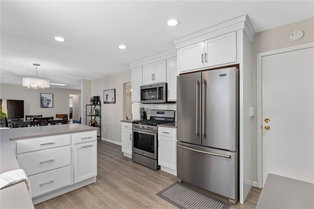 kitchen with stainless steel appliances, white cabinets, light countertops, light wood finished floors, and decorative light fixtures