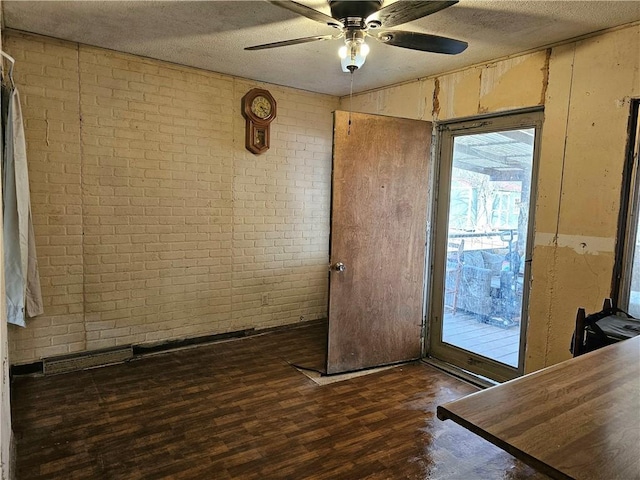 doorway with ceiling fan, brick wall, dark hardwood / wood-style floors, and a textured ceiling