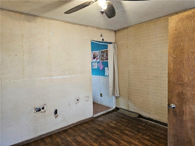 laundry area featuring dark wood-type flooring, ceiling fan, brick wall, and a textured ceiling