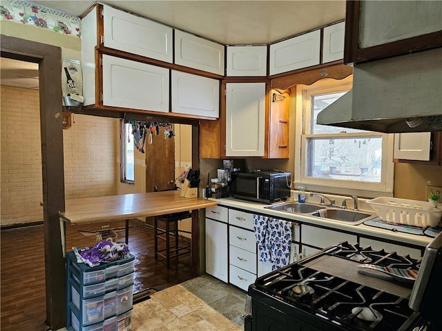 kitchen featuring brick wall, range with gas stovetop, sink, and white cabinets