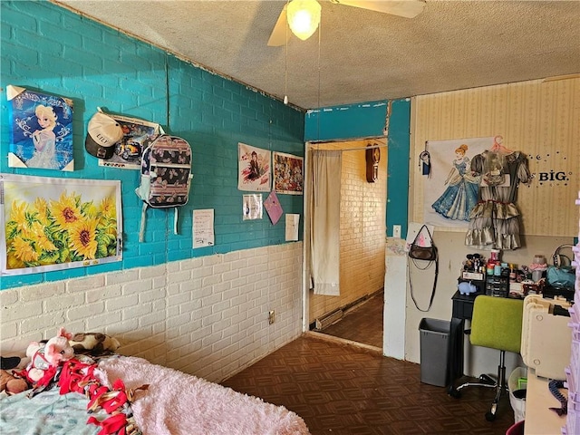 bedroom featuring ceiling fan, brick wall, dark parquet floors, and a textured ceiling