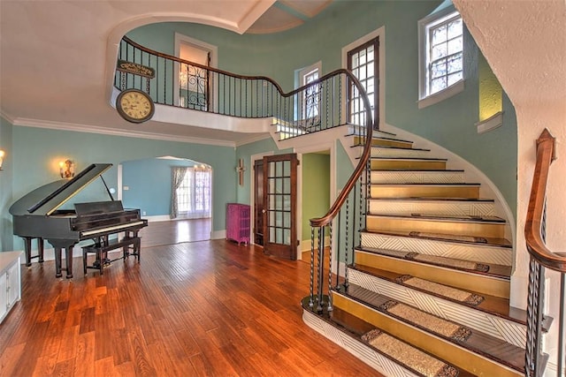 stairway with arched walkways, crown molding, a high ceiling, wood finished floors, and baseboards