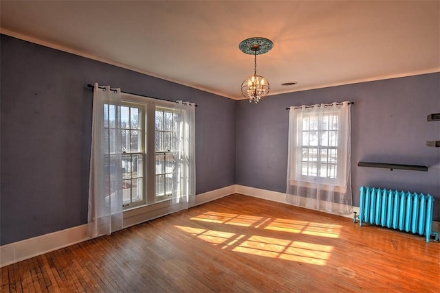 spare room with a notable chandelier, wood finished floors, baseboards, ornamental molding, and radiator heating unit