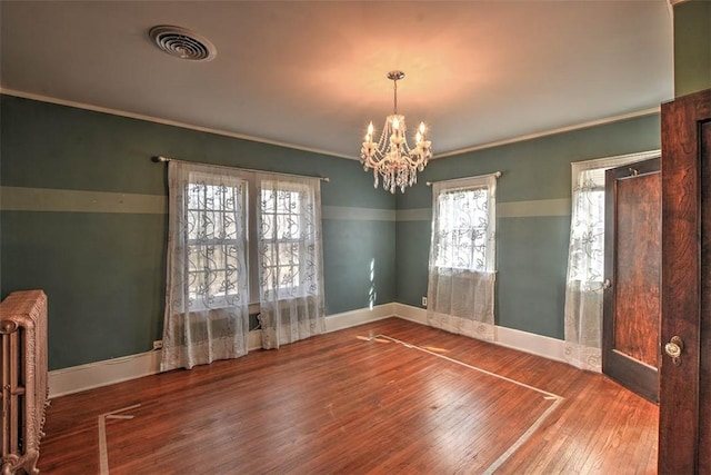 unfurnished room featuring wood finished floors, visible vents, baseboards, ornamental molding, and radiator