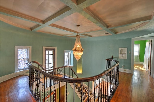 hall with baseboards, coffered ceiling, wood finished floors, and an upstairs landing