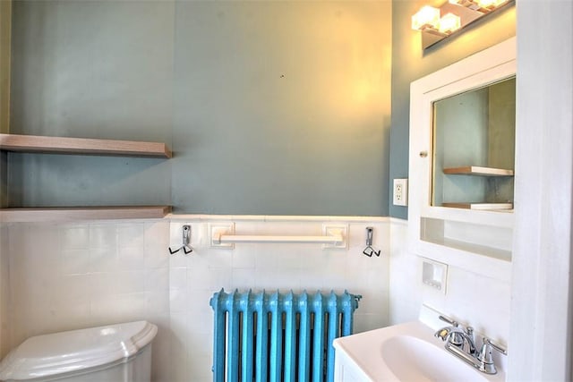 half bath with radiator, a wainscoted wall, toilet, and a sink