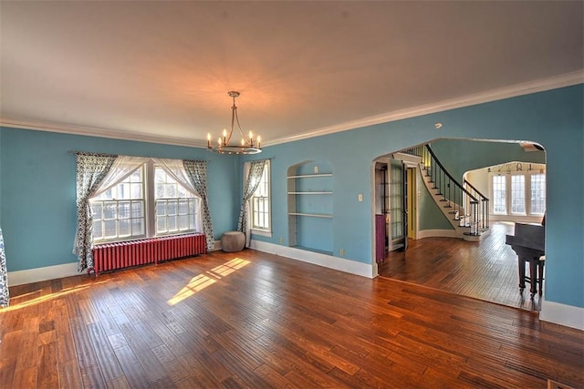 spare room featuring arched walkways, a chandelier, wood finished floors, stairway, and radiator heating unit