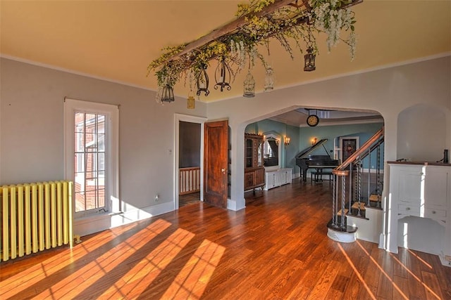 interior space featuring arched walkways, radiator, stairway, wood finished floors, and crown molding