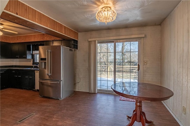 kitchen with dark wood-type flooring, sink, high quality fridge, wooden walls, and ceiling fan with notable chandelier