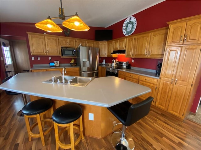 kitchen featuring stainless steel appliances, a sink, wood finished floors, under cabinet range hood, and a kitchen bar