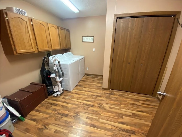 washroom with a textured ceiling, washer and clothes dryer, light wood-type flooring, and cabinet space