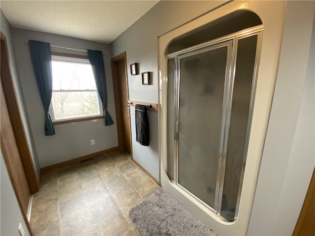 bathroom featuring a stall shower, visible vents, a textured ceiling, and baseboards