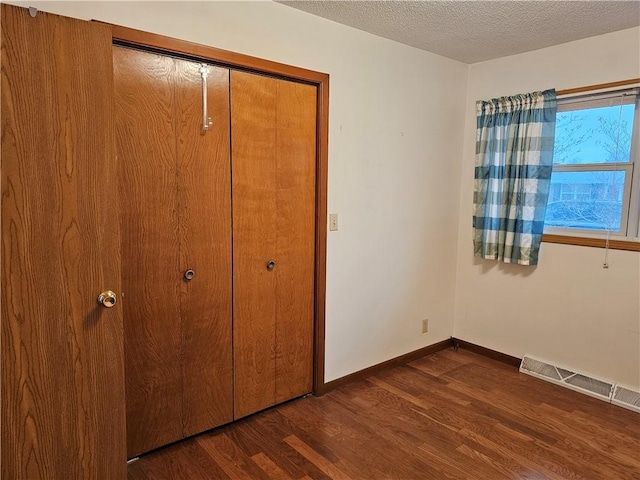 unfurnished bedroom with a textured ceiling, a closet, and dark wood-type flooring