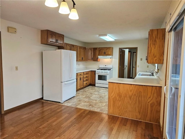 kitchen with kitchen peninsula, white appliances, light hardwood / wood-style floors, and sink