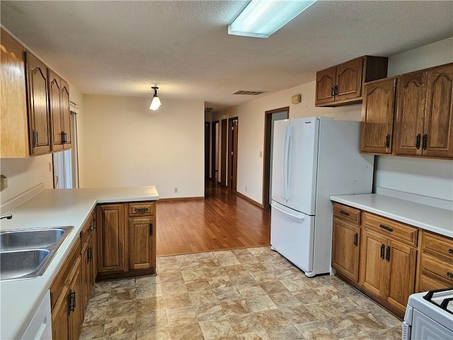 kitchen with kitchen peninsula, light wood-type flooring, white appliances, sink, and hanging light fixtures