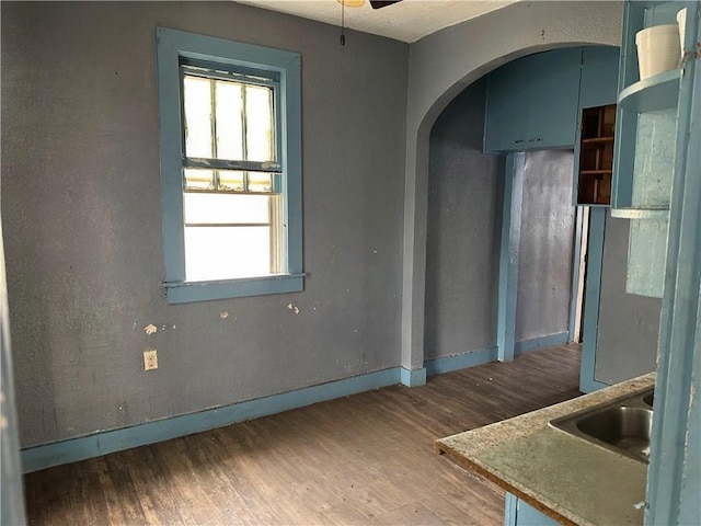 empty room with a sink, wood finished floors, baseboards, ceiling fan, and arched walkways