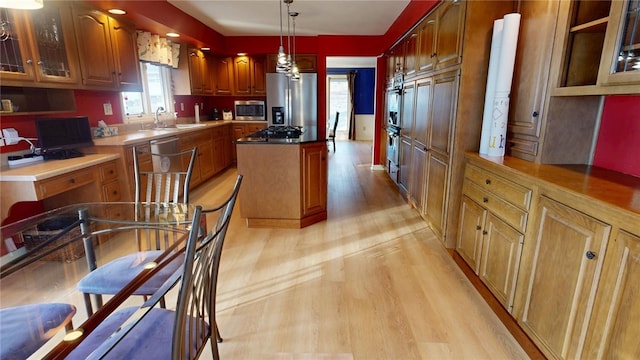 kitchen with appliances with stainless steel finishes, decorative light fixtures, sink, a center island, and light hardwood / wood-style flooring