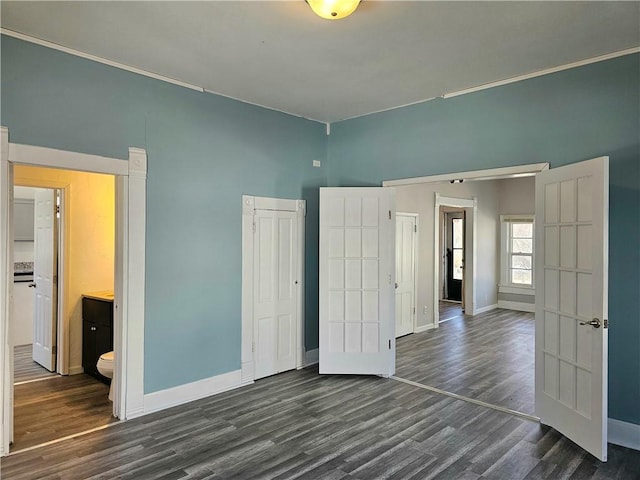 unfurnished bedroom with baseboards, ensuite bath, dark wood-style floors, and crown molding