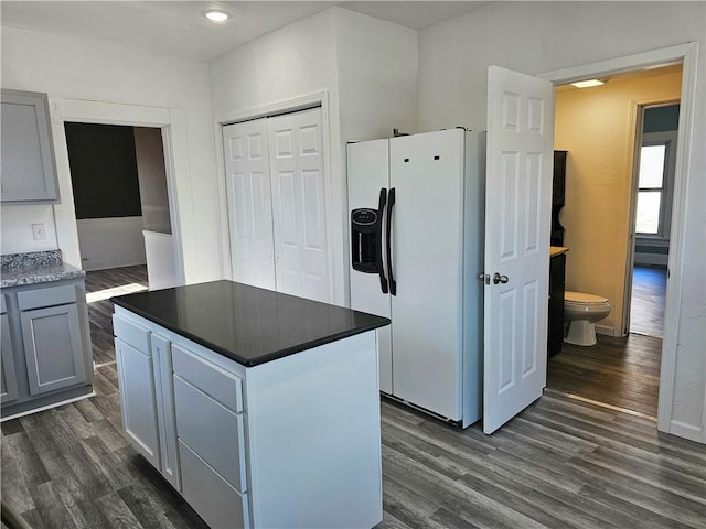 kitchen with dark countertops, a kitchen island, gray cabinets, white fridge with ice dispenser, and dark wood-style floors