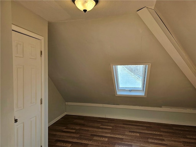 bonus room with lofted ceiling with skylight and dark wood-type flooring