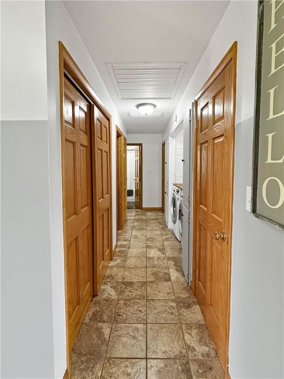 corridor featuring washer and dryer, light stone finish flooring, attic access, and baseboards