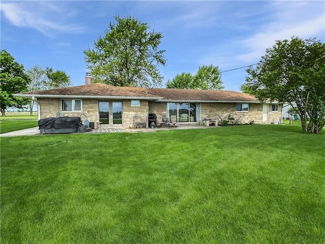 rear view of house with stone siding, a chimney, a yard, and a patio