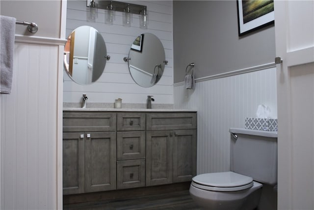 bathroom with wooden walls, vanity, wood-type flooring, and toilet