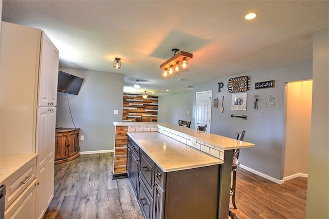 kitchen featuring a breakfast bar, a center island, dark hardwood / wood-style floors, a textured ceiling, and white cabinetry