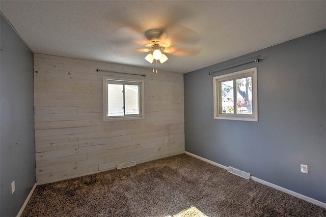 unfurnished room with carpet flooring, a textured ceiling, ceiling fan, and wooden walls