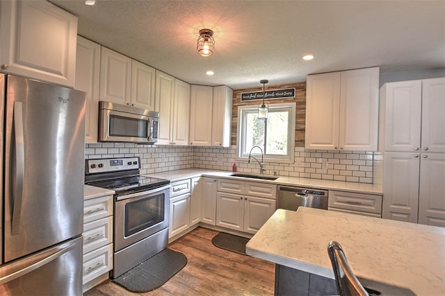 kitchen featuring appliances with stainless steel finishes, dark hardwood / wood-style flooring, sink, decorative light fixtures, and white cabinets